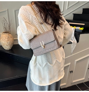 Close-up of grey crocodile embossed crossbody bag with golden chain strap on model