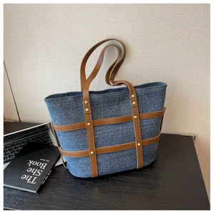 Close-up of denim tote bag with brown leather lattice and gold rivet stud details