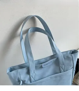 Detail of light blue tote bag with durable reinforced shoulder strap stitching and leather tag