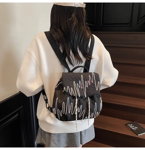 Detail of black backpack with textured pleats and colorful wavy embroidery on the flap