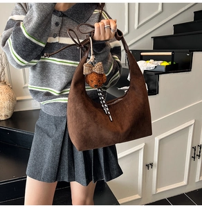 Detail view of brown suede crescent moon bag featuring a plush bear charm on its side