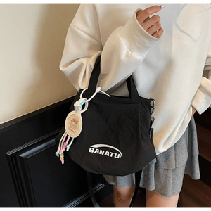 Close-up of black canvas shoulder bag with white logo print and a beaded capybara charm
