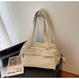 Detail view of beige nylon shoulder bag with front zipper pocket and wide fabric strap