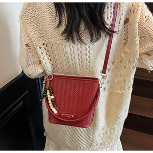 Red woven texture bucket bag shown with a wooden bead charm and metal logo plaque