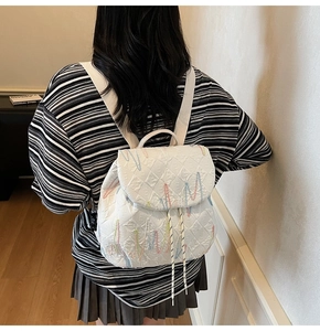 Detail of white quilted leather backpack with colorful embroidery and drawstring closure