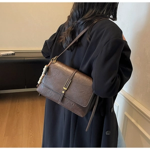 Brown oil wax leather shoulder bag with gold clasp and wooden bead charm on model