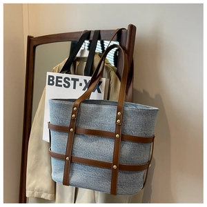Close-up of washed denim tote with brown leather lattice and gold rivet accents
