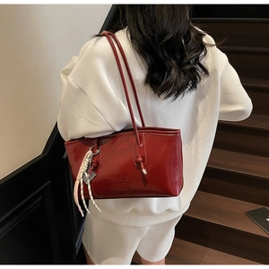 Detail of red glossy tote bag featuring brand embossing and contrast braided strap