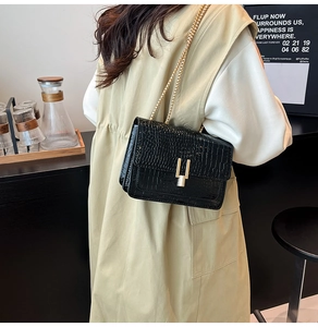 Detail view of the black faux crocodile texture and gold U-shaped metal buckle on the bag