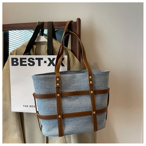 Detail view of denim tote bag featuring brown leather straps and gold metal rivet accents