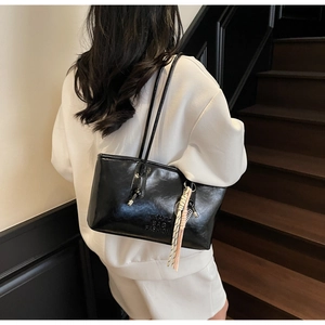Detail of black glossy PU leather tote bag with embossed text and woven rope charm