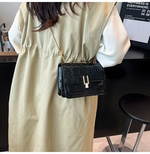 Close-up of black crocodile pattern crossbody bag with gold U-shaped lock and chain
