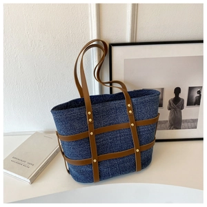 Close-up of vintage denim tote bag with brown leather straps and gold rivets