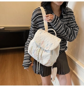 Detail view of white quilted mini backpack with colorful embroidery on a model