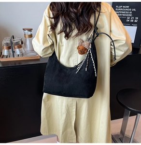 Detail of black suede crescent bag with plush bear charm and woven rope accents