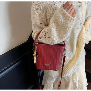 Detail view of red woven bucket bag with beaded charm and gold-tone metal emblem