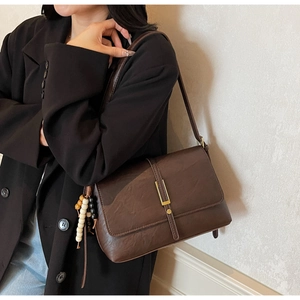 Détail d'un sac bandoulière marron foncé avec boucle dorée et perles porté par un modèle