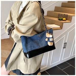 Detail of denim and leather tote bag with chain strap and bear charm on stairs