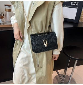 Close-up of black crocodile embossed leather bag with gold chain and H-shaped clasp