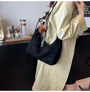 Close-up of black suede hobo bag featuring a brown plaid bear charm and woven rope detail