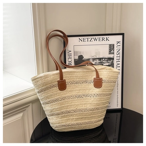 Detail of cream woven tote bag featuring brown leather shoulder straps and textured fiber