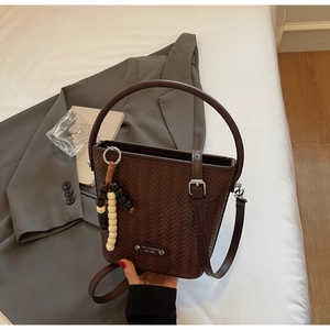 Detail of a brown woven bucket bag with wood bead tassel on a stylish white background