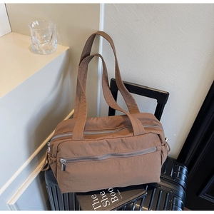 Detail of a large capacity brown nylon tote bag with multi-zipper pockets on a black suitcase