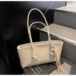 Detail of off-white tote bag featuring embossed logo and braided tassel on a black book