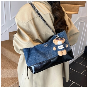 Detail of denim tote bag with leather patchwork, chain strap and a cute bear charm