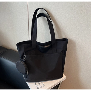 Close-up of minimalist black tote bag with front pocket and detachable round coin purse