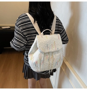 Detail view of white quilted backpack featuring colorful wavy embroidery and drawstring top