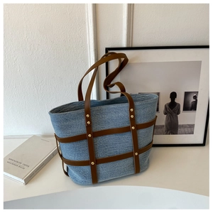 Detailed shot of blue denim tote bag with brown leather grid and gold rivets on a desk