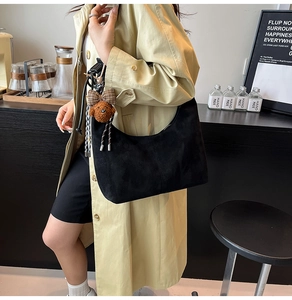 Detail of black suede hobo bag with a cute brown plush bear keychain on beige coat