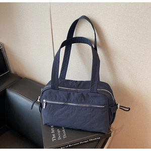 Detail of navy nylon tote bag showing textured fabric and silver zipper on leather sofa