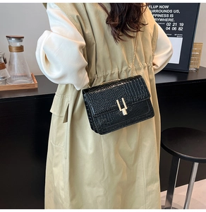 Detail of black crocodile-textured crossbody bag with elegant gold chain strap and U-shaped lock