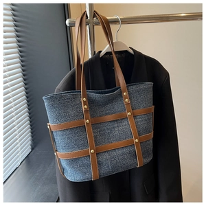 Detail of vintage denim tote bag with brown leather handles and gold rivet accents