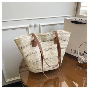Detail shot of the cream woven tote bag with brown straps on a wooden table in a lifestyle setting