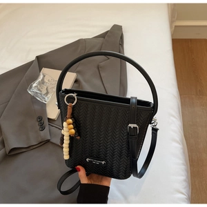 Detail of black woven bucket bag showing beaded charm and metal logo on smooth leather