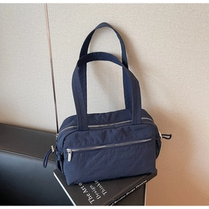 Detail of navy blue nylon tote bag showing dual zippers and front pocket on book prop