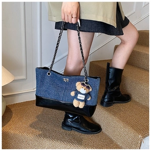 Detail of denim tote bag with leather patchwork, metal chain strap and bear charm