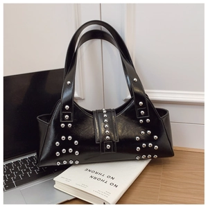 Detail of black glossy leather shoulder bag with silver rivet studs on a desk