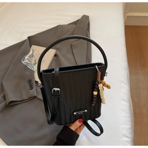 Detail of black woven bucket bag with beaded charm and branded plaque on a modern setting