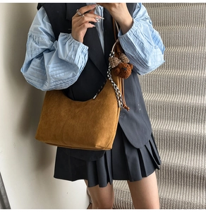 Detail of brown suede hobo bag with a plush bear charm and plaid bow on the side