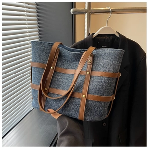 Close-up of denim tote bag featuring brown leather straps and decorative gold studs