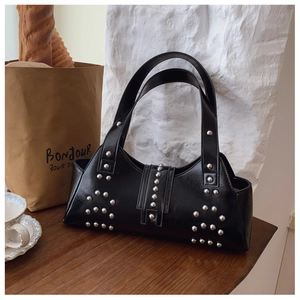 Detail of black matte leather shoulder bag with silver punk style rivets on a wooden table