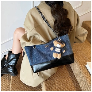 Detail of denim and black leather tote bag with stylish teddy bear charm accessory