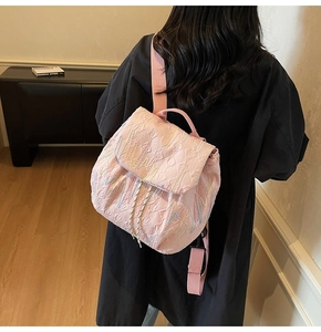 Rear view of a pink quilted mini backpack with wavy embroidery worn by a model