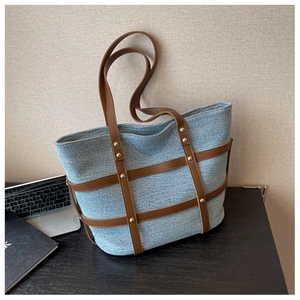 Detail of blue denim tote bag with brown leather lattice frame and gold rivets