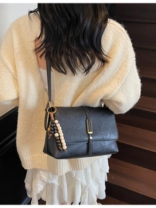 Vintage black leather flap crossbody bag with wood bead charm and gold buckle on model
