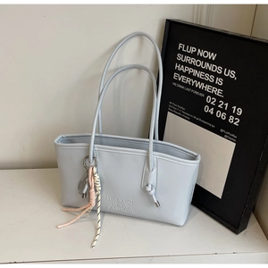 Close-up of light blue leather tote bag featuring a brand logo and a tennis racket charm